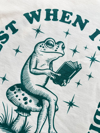 Frog reading a book on a mushroom with text and stars around, on a light background