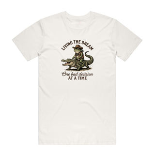 White t-shirt with a graphic of a person riding a dinosaur and text 'Living the Dream, One bad decision at a time' on a white background.